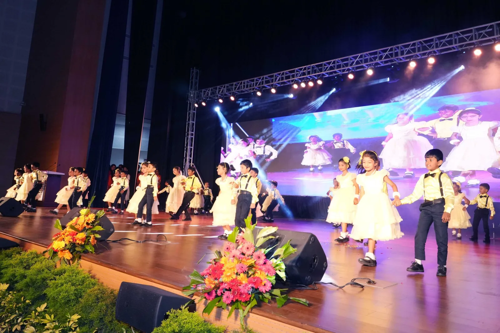 Students in blue costume performing on the Annual Day stage under dramatic lighting