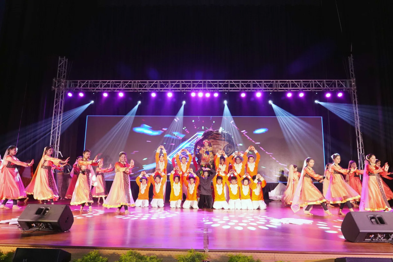A large group of students in formation performing a dance on the Annual Day stage