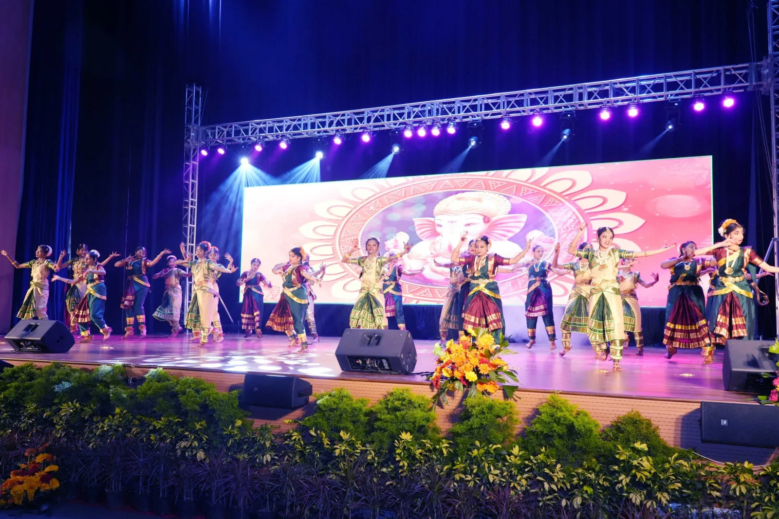 Students performing a traditional dance in front of an elephant-themed stage backdrop