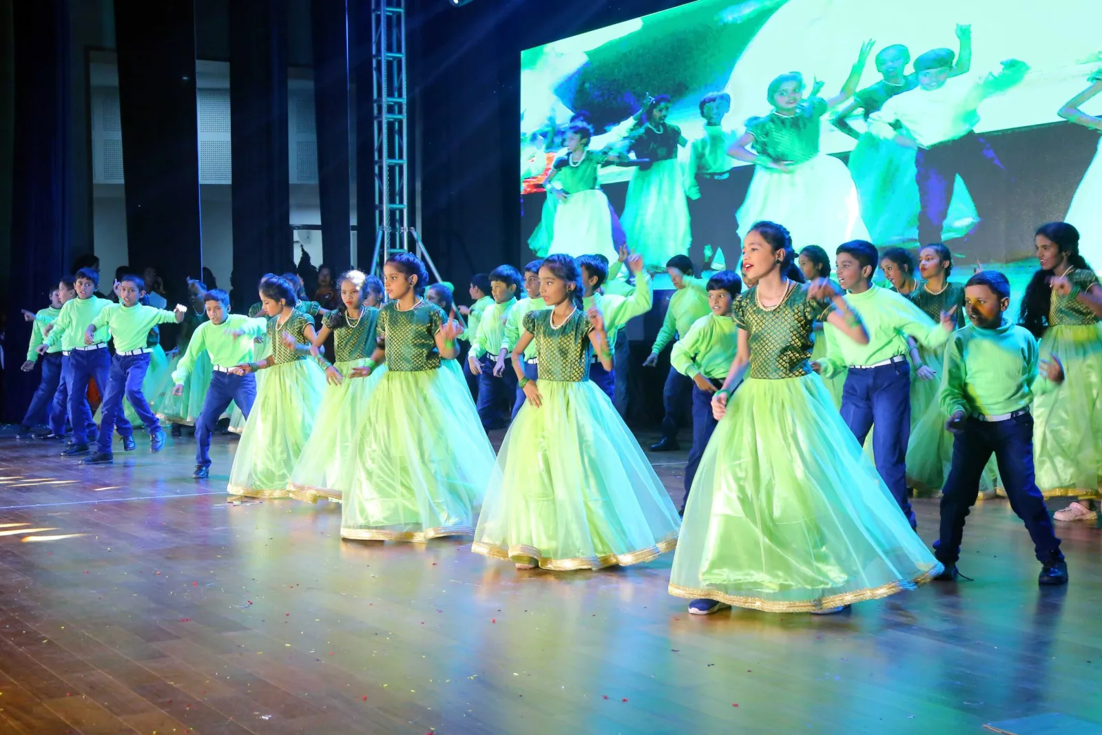 A choir of students in pink and red costume performing on the Annual Day stage