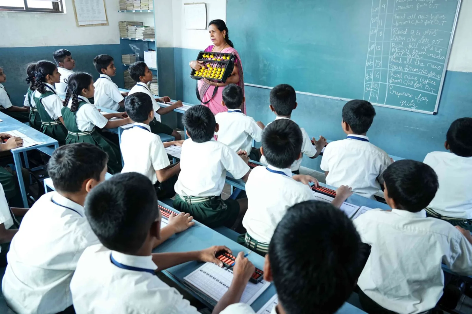 A teacher demonstrating an abacus at the front of a classroom while seated students follow along with their own abacus frames