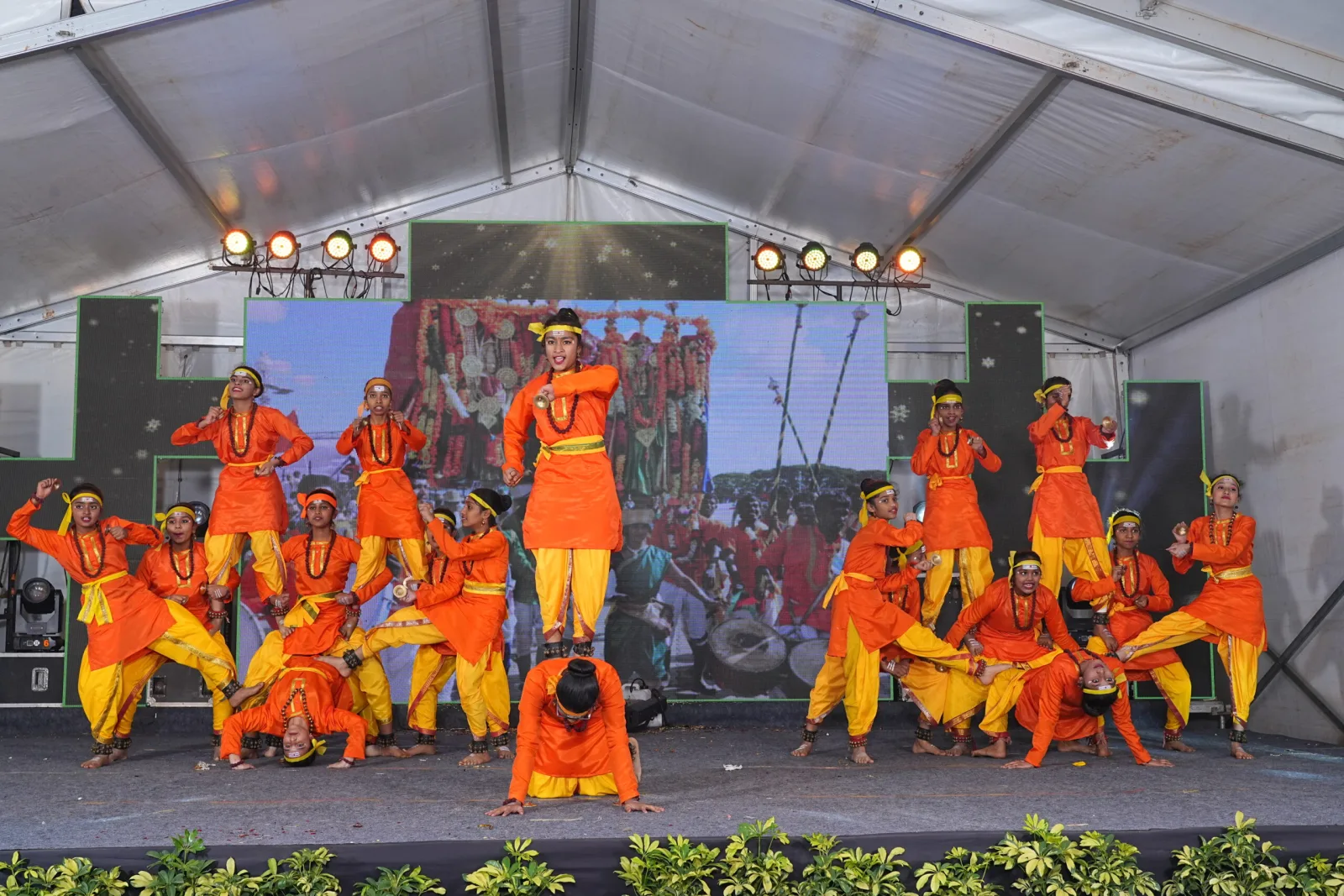 Students in orange and red costume performing a dramatic dance on stage