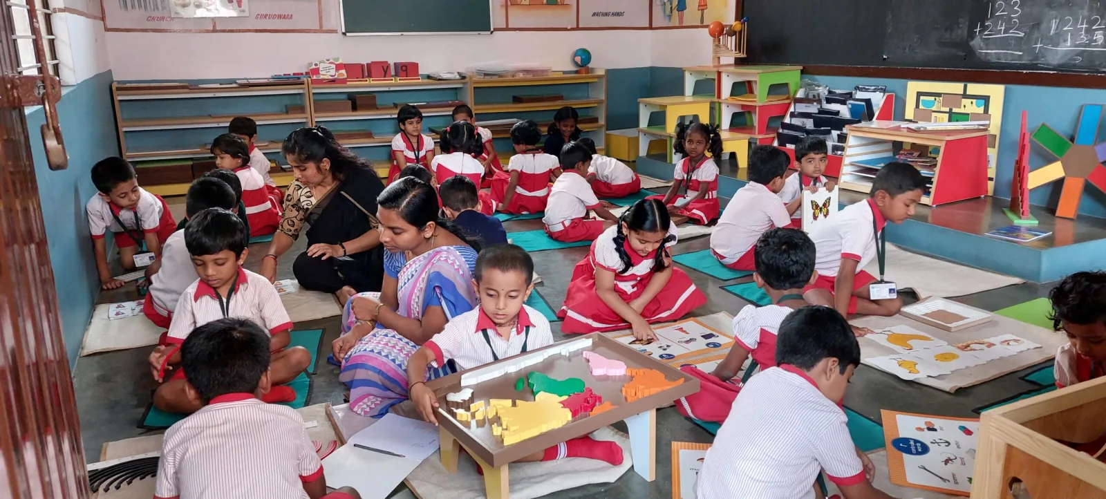 Young children seated on mats engaged in hands-on Montessori learning activities with a teacher
