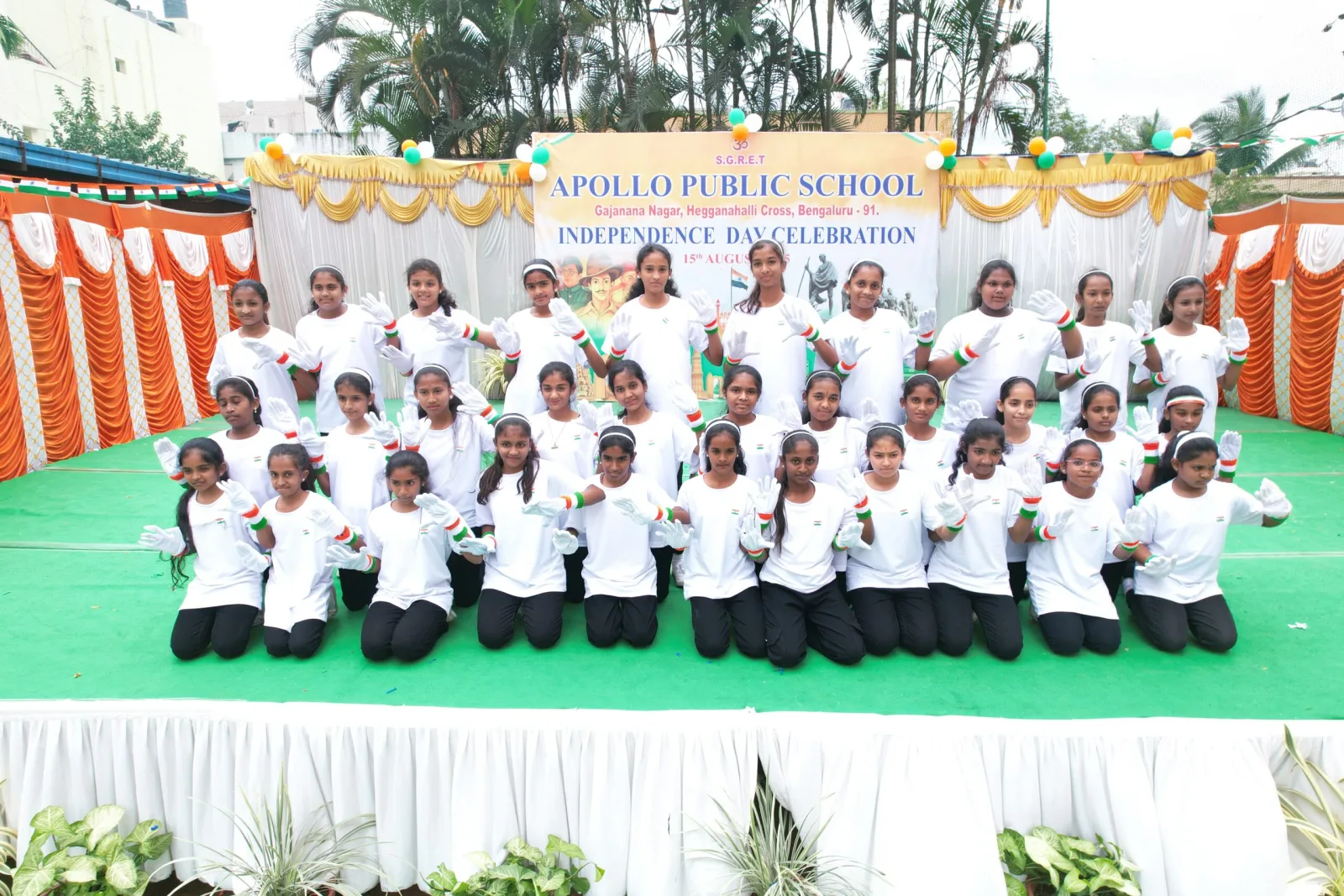 A large group of students in white uniform posing together on an outdoor stage