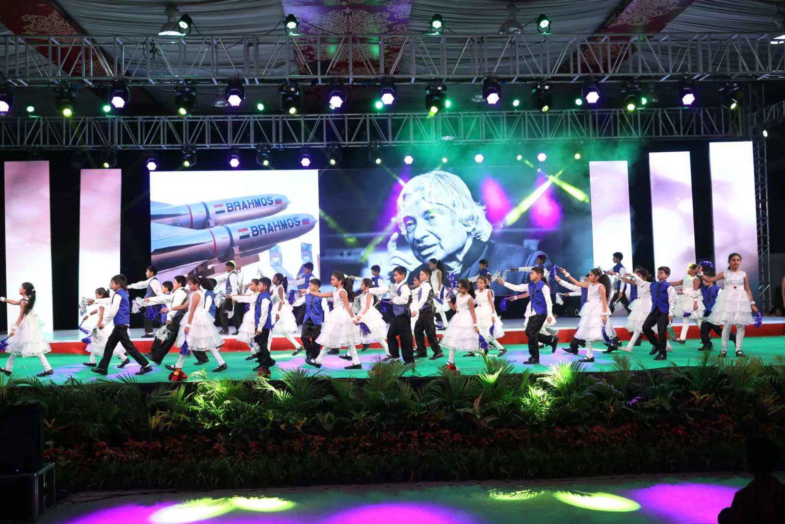 A large group of students performing a choreographed dance in front of a globe-themed stage backdrop