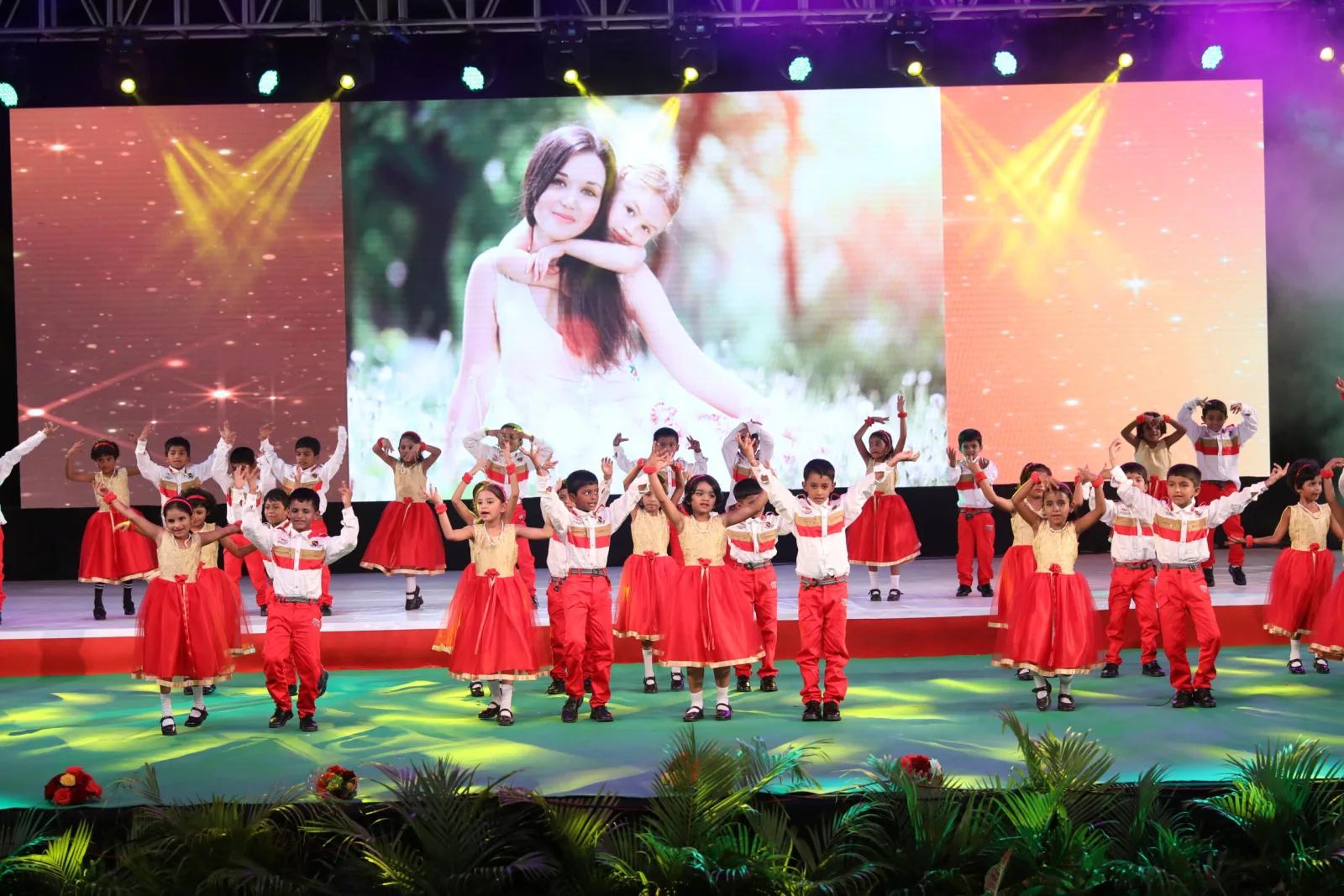 Students in red and white costume performing a dance on a brightly lit stage