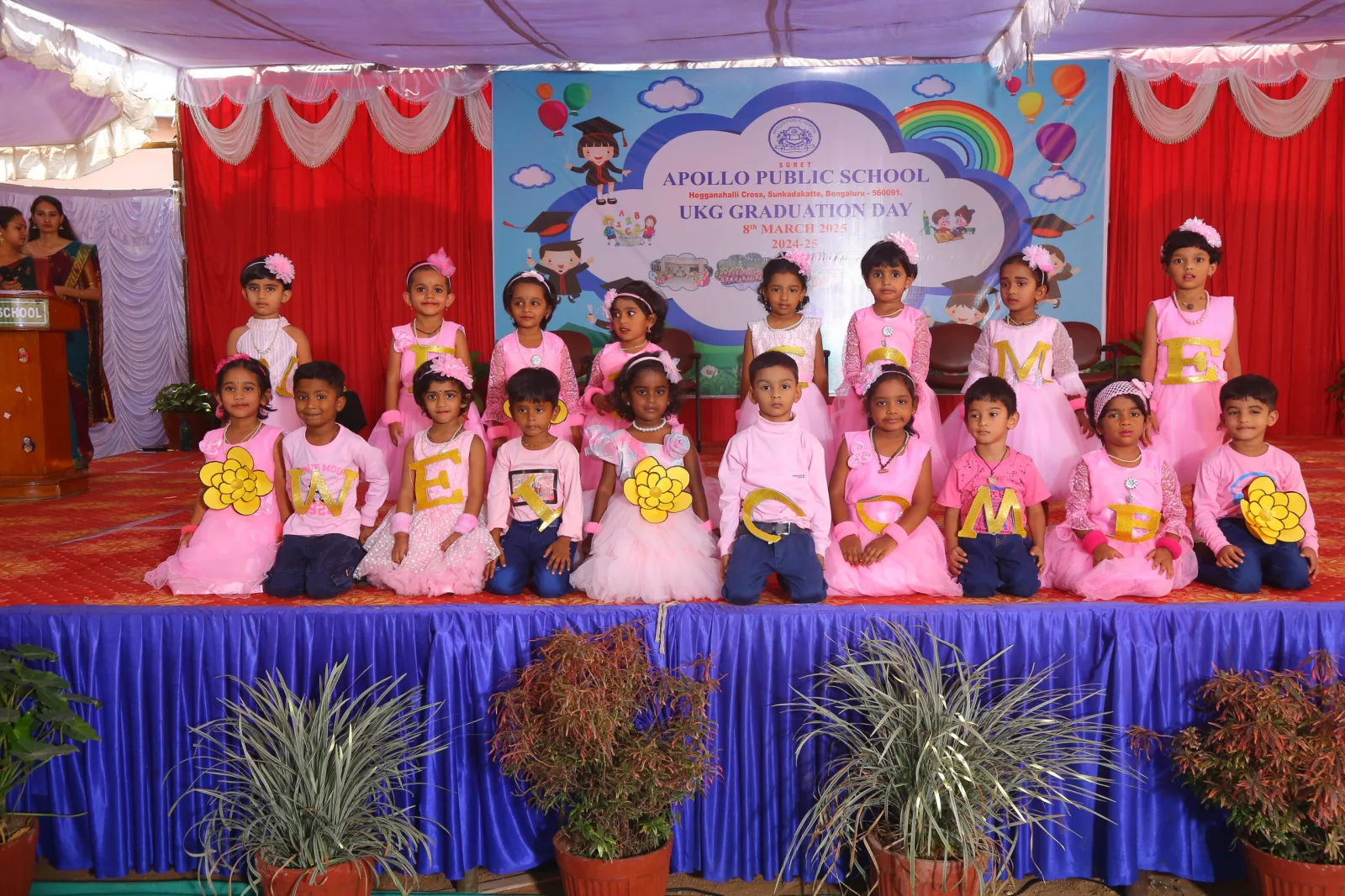UKG children in pink dresses posing together on a decorated stage